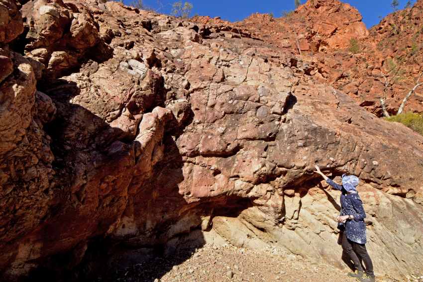 Photograph of a woman dressed in blue, pointing towards a rock formation in the outback