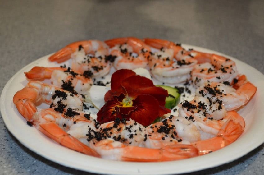 Photograph of a plate of cooked prawns garnished with a red flower and tiny black ants