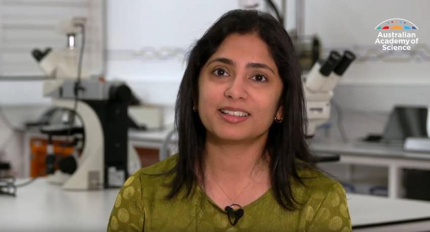 A woman wearing a gold shirt smiles at the camera in a lab