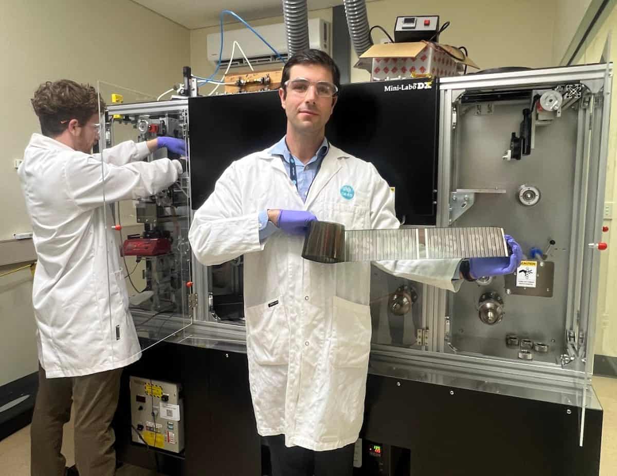 A man in a labcoat shows a roll of solar cells to the camera.