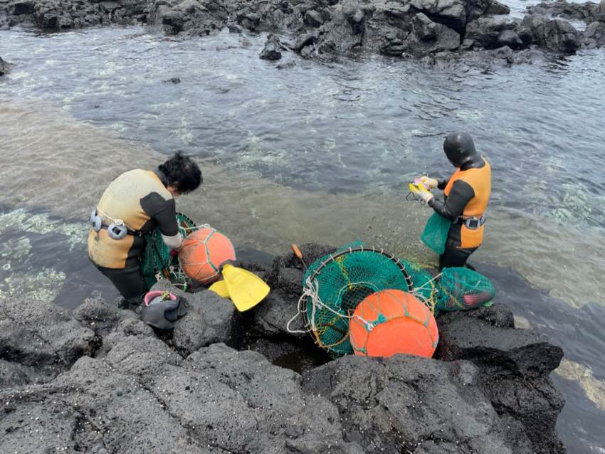 Women dressed head to toe in wetsuits prepare diving nets next to the sea