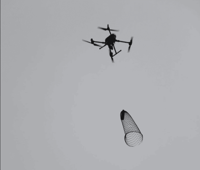 A drone drops a water bottle attached to a net-like parachute