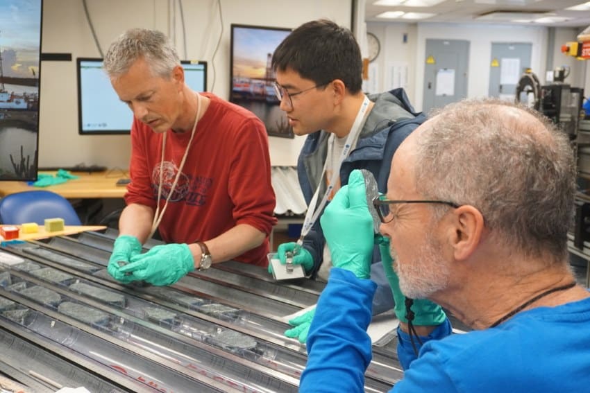 A photograph of 3 researchers examining lengths of rock