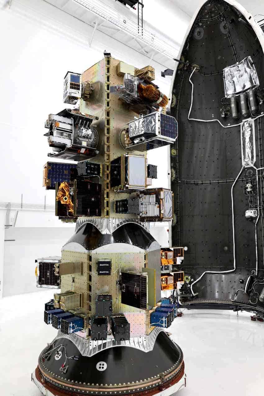 A photograph of the inside of a rocket casing showing dozens of small cube-shaped satellites mounted to a central column