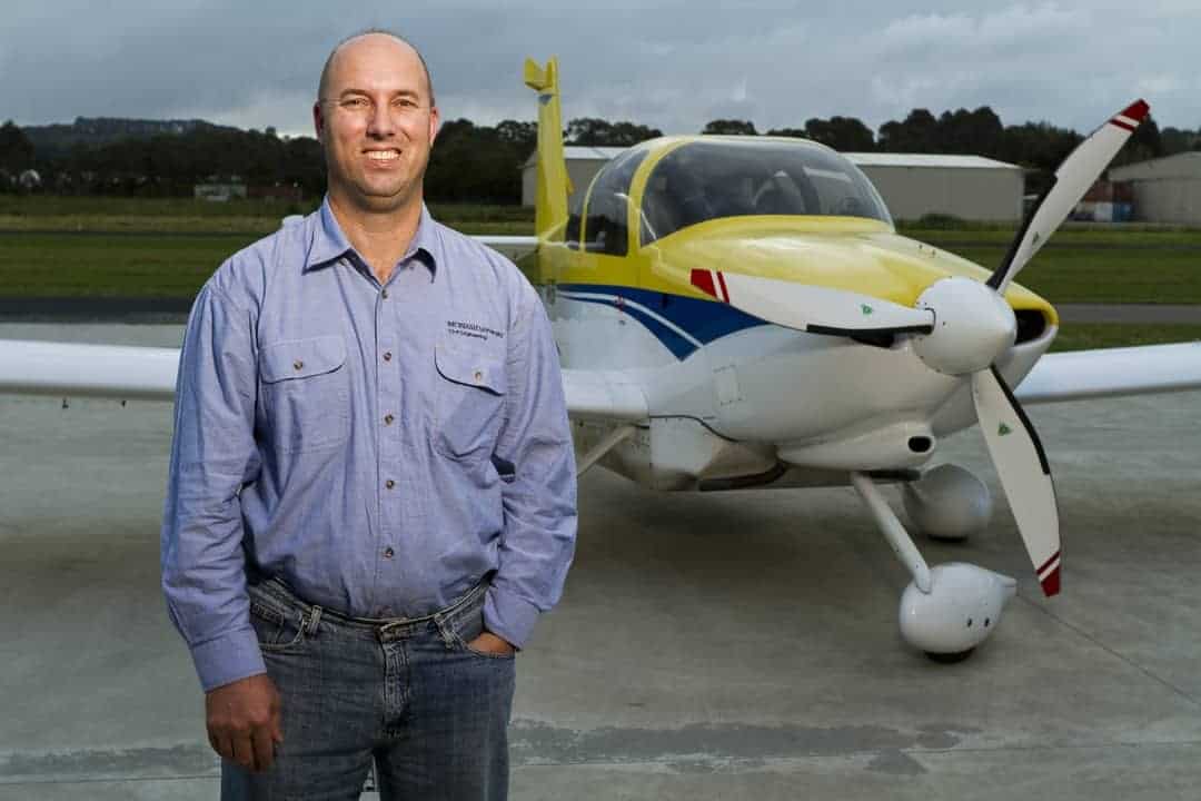A photograph of a man wearing a blue shirt standing in front of a light plane