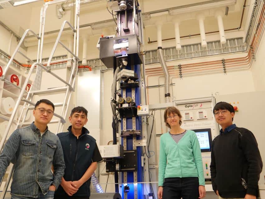 A photograpjh of 3 young men and a woman standing in front of a tall tower-like piece of equipment inside of a lab