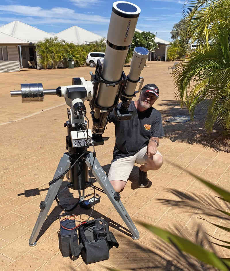 Man crouching next to telescope on sunny day in suburb