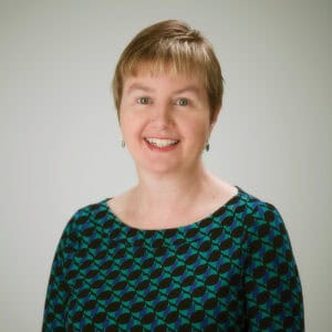Woman with short hair and earrings, wearing green and black top.