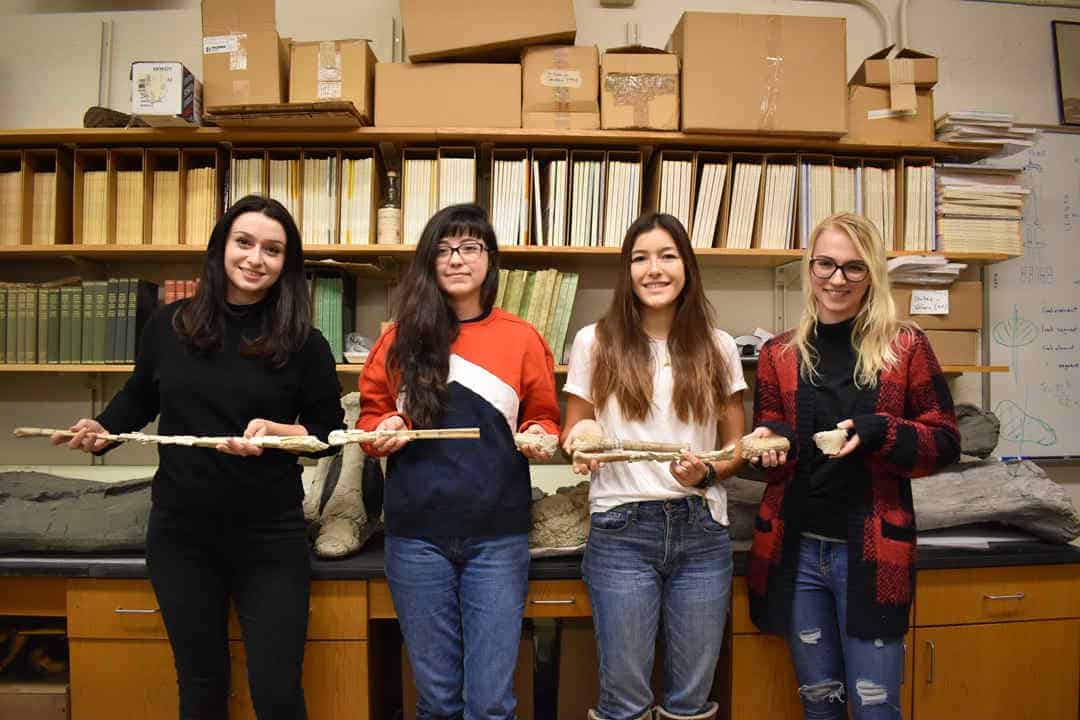 Four palaeontologists hold long fossil bone