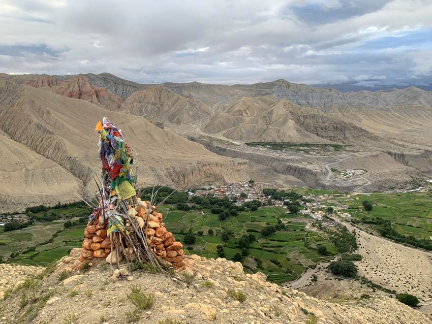 A photo looking over a village in the distance from a high mountain, uin the foreground is some kind of man-made rock, stick and fabric marker
