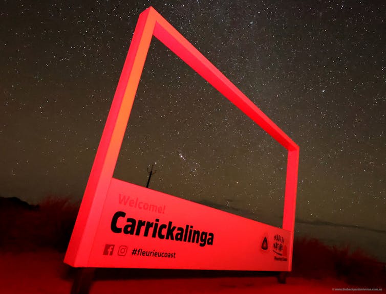 A photograph of an illuminated red frame that says "welcome! Carrickalinga". The night sky can be seen in the background.