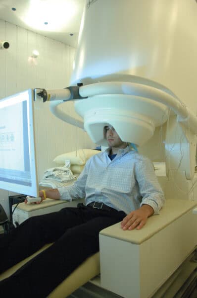 Man in shirt and pants in a large white machine scanning head.