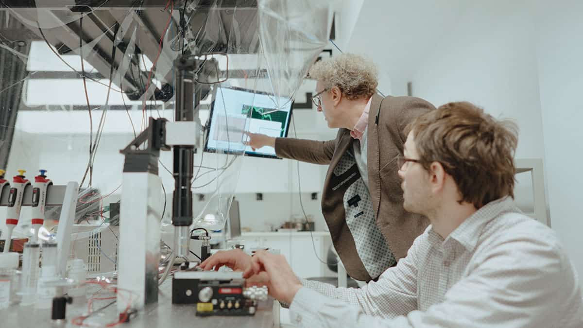 Two men, each wearing glasses, looking at a screen in a lab.