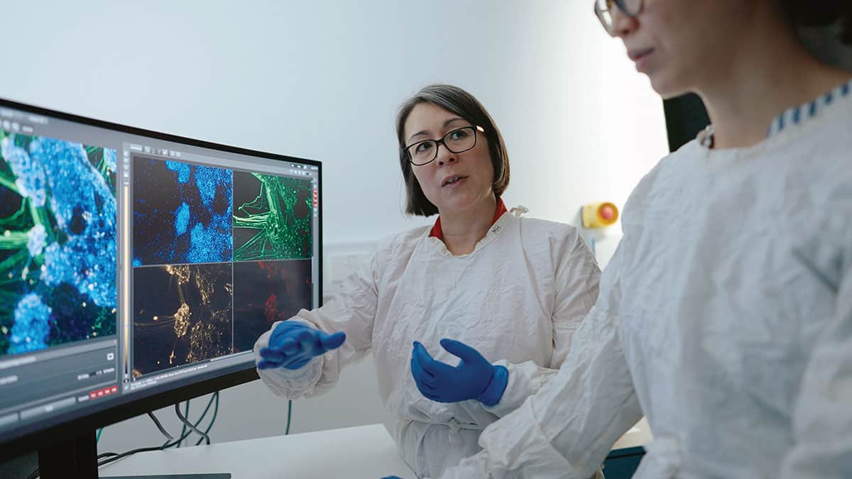 Two women in ppe next to a screen discussing biological images.