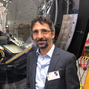 Man wearing glasses and a suit in front of astronomy equipment.