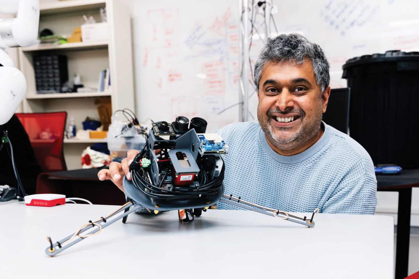 Man in blue jumper behind a desk with a robot on it.