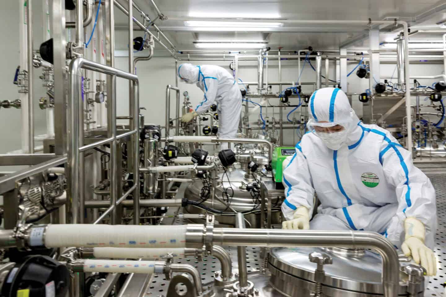 Two people in protective wear checking a bioreactor that looks like machinery.
