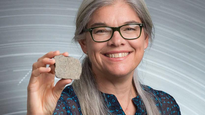 Woman with silver hair and black glasses holding a rock.