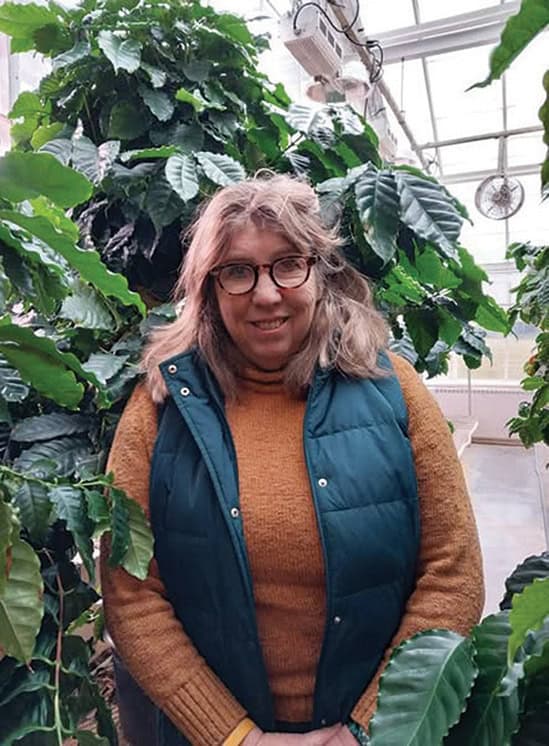 Woman wearing a vest in a greenhouse filled with plants.