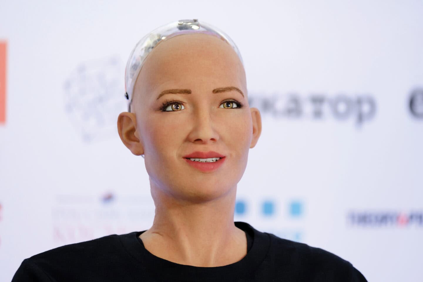 Robot with human-like face and skin wearing a black t-shirt.