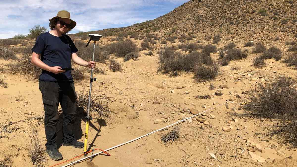 Archaeologist in t shirt and hat in arid africa with survey equipment