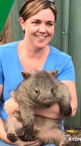 A woman wearing a blue tshirt holds a wombat in front of herself