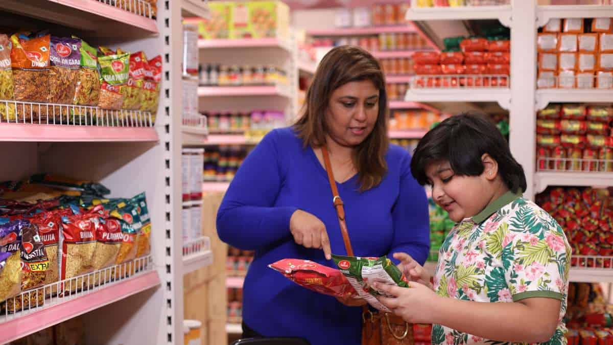 A woman and young boy deliberate between 2 packets of food in a supermarket.