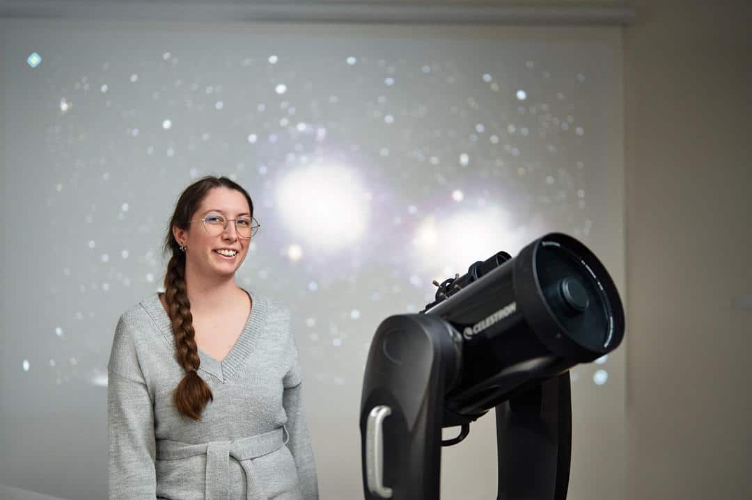 Astronomer in grey sweater in front of stars image with telescope