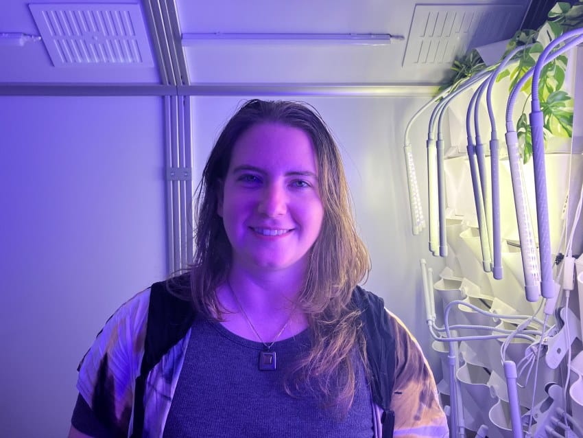 A woman stands inside a white, futuristic room filled with purple lighting