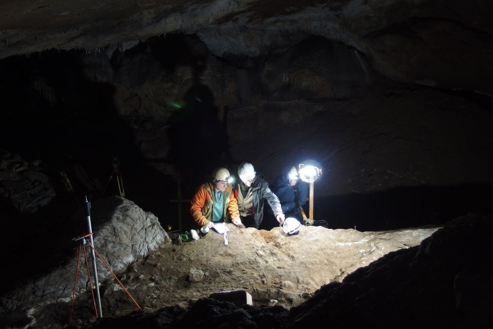 Two people in hard hats in dark cave excavation site