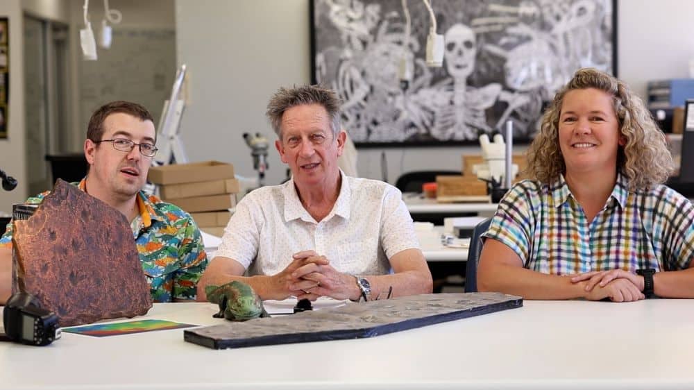 Three researchers sitting at table bench with fossil trackway footprints
