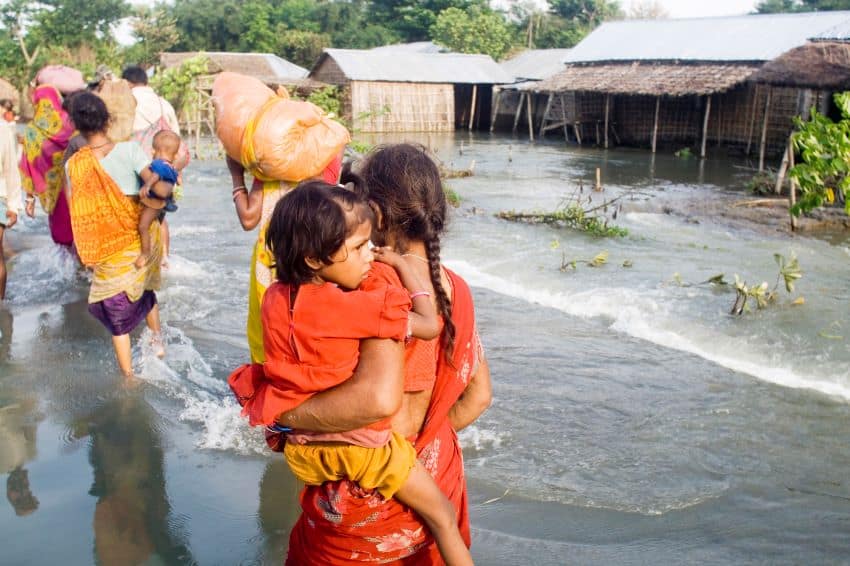 A line of people carrying children and goods above floodwaters in india.
