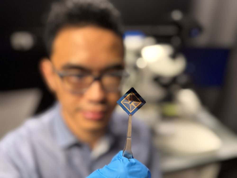 Blurred researcher with glasses and blue gloves holds tiny device with tweezers