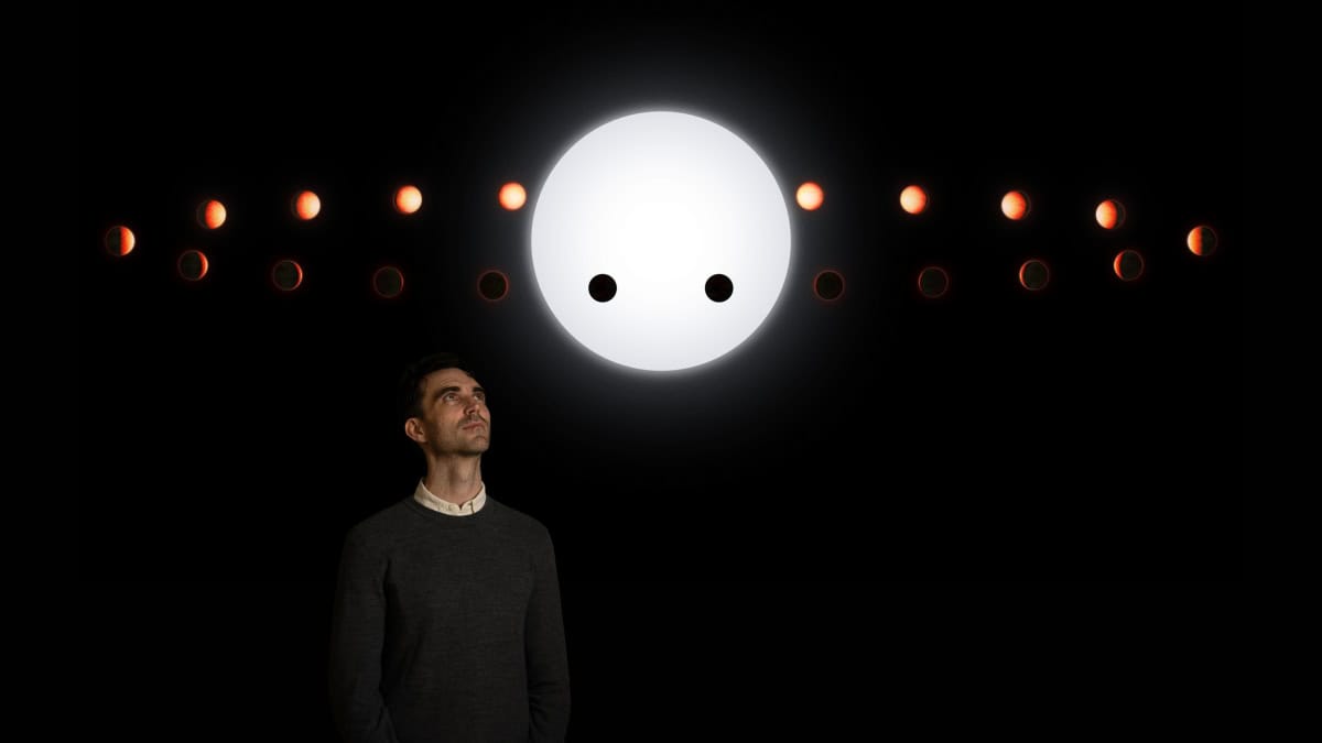 A man looking up at orbiting planet around star on black background