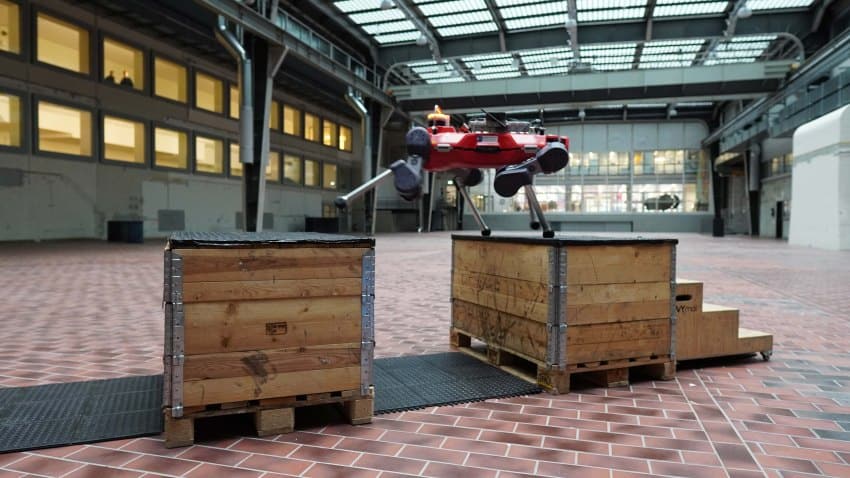 A red 4-legged robot strides from one wooden box across a gap to another