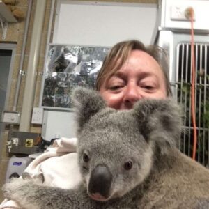 A woman with light blonde hair holds a koala on her front