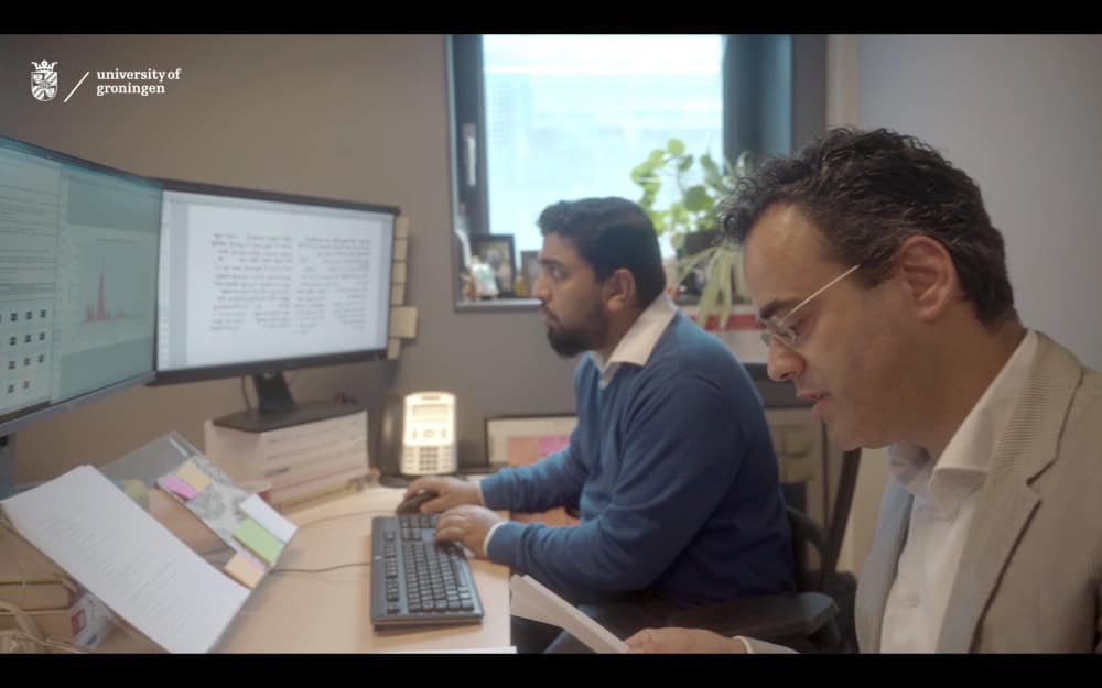Two men in front of computer monitors looking at ancient writing