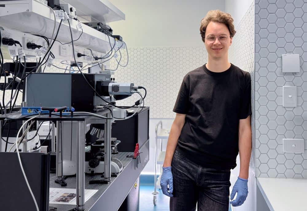 Person with blue gloves and black top next to complicated lab equipment