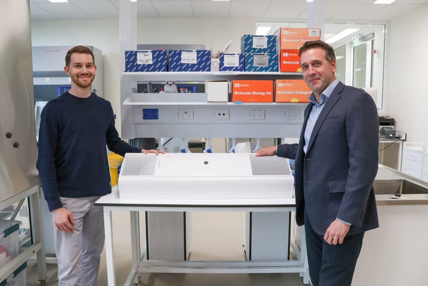 Two men standing in a lab with a rectangular, white piece of techology