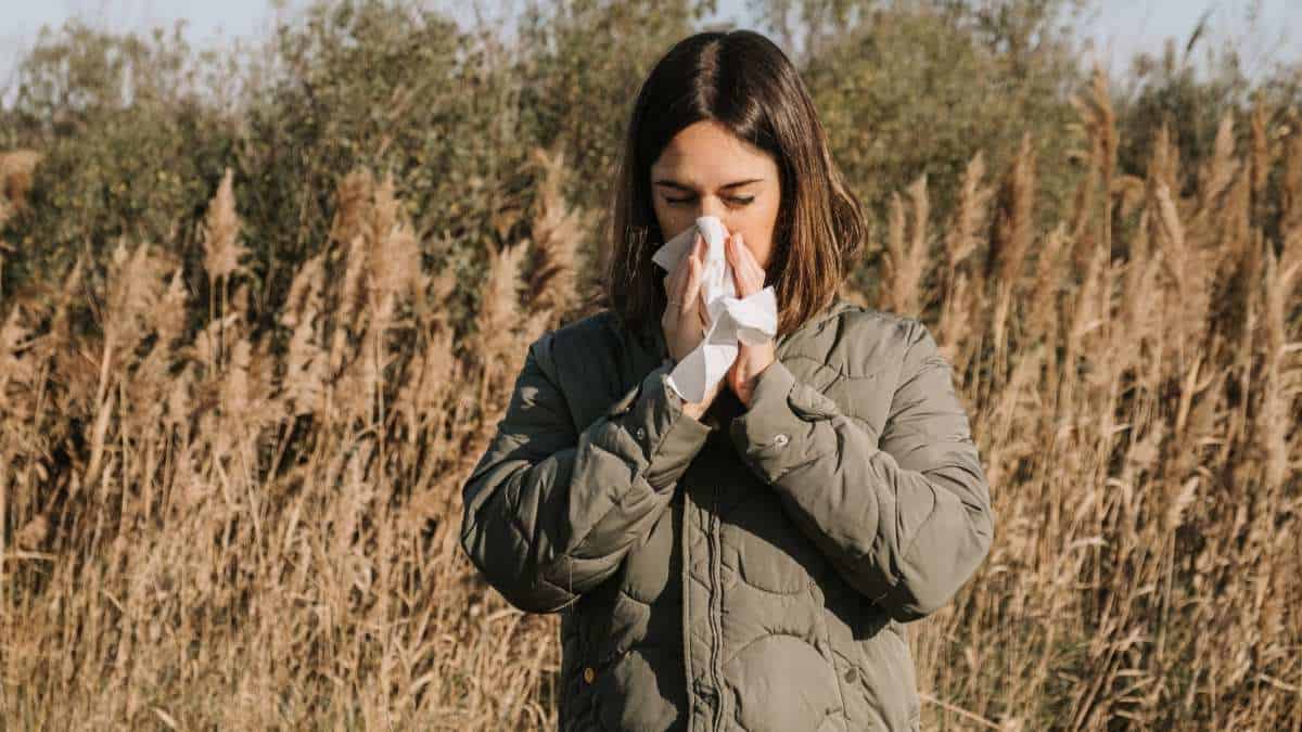 Adult woman suffering spring allergy and blowing nose with a tissue in the nature