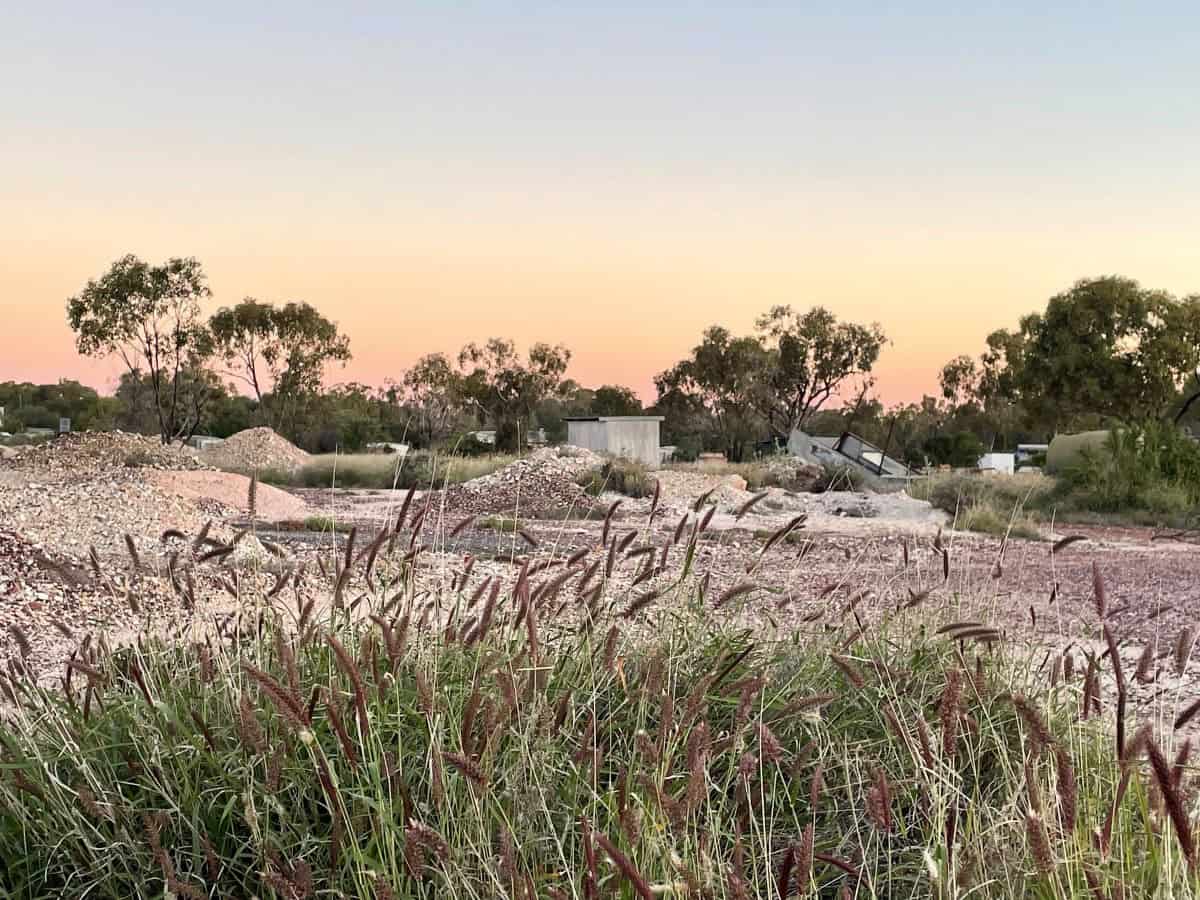 Landscape with mounds of rubble, sunrise and grassy foreground.