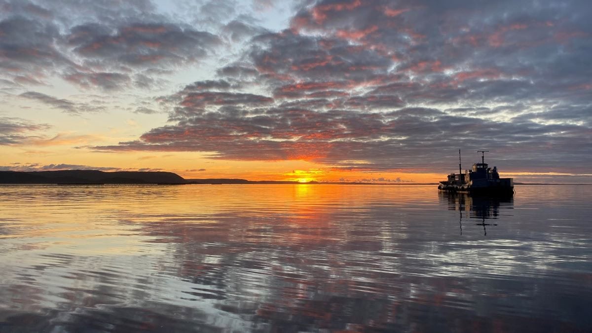 Barge anchored in still water with sunset in the background.