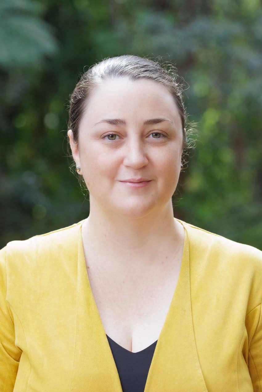 Headshot of a woman with brown hair tied back wearing a yellow blazer.