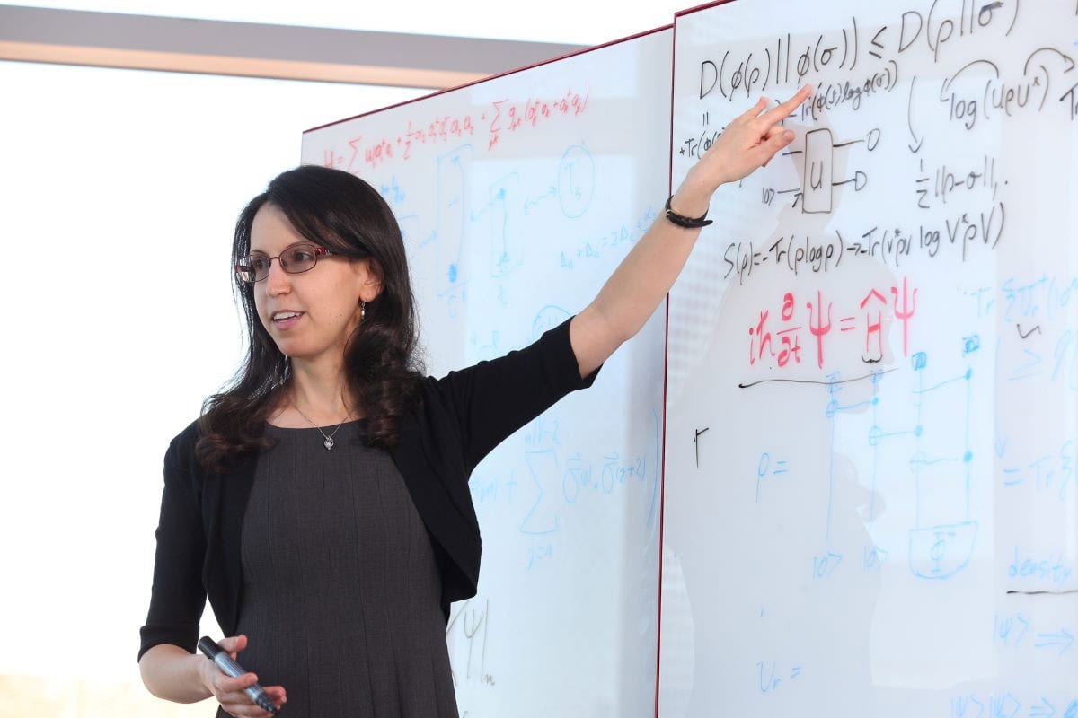 Woman pointing at equations written on a white board.