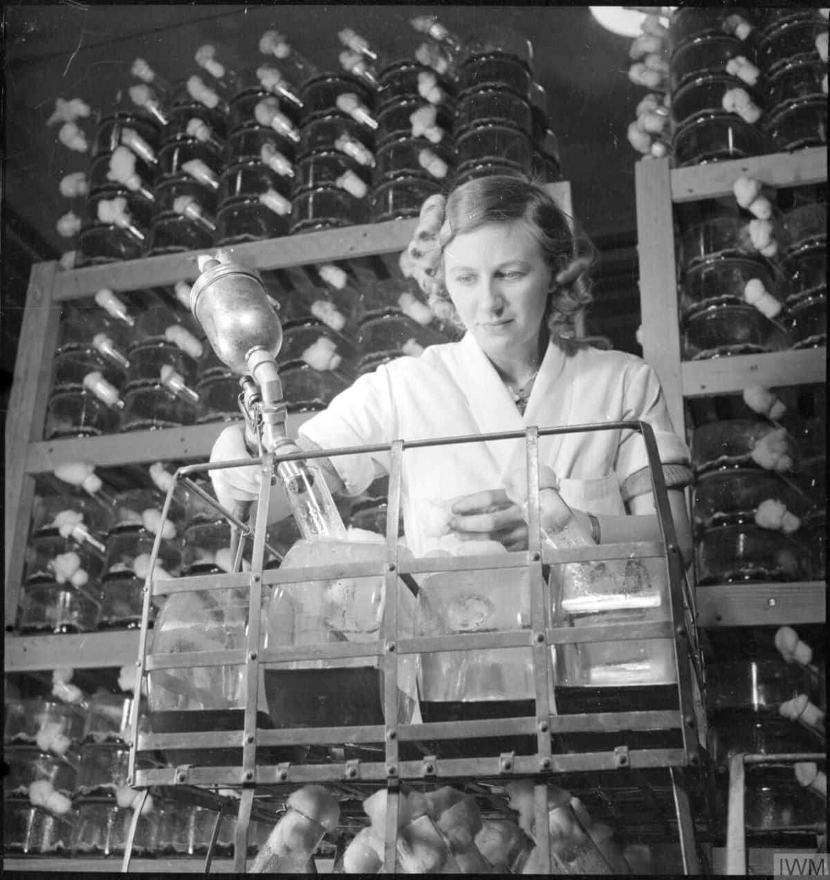 A lab worker filling vessels with a wall of vessels behind.