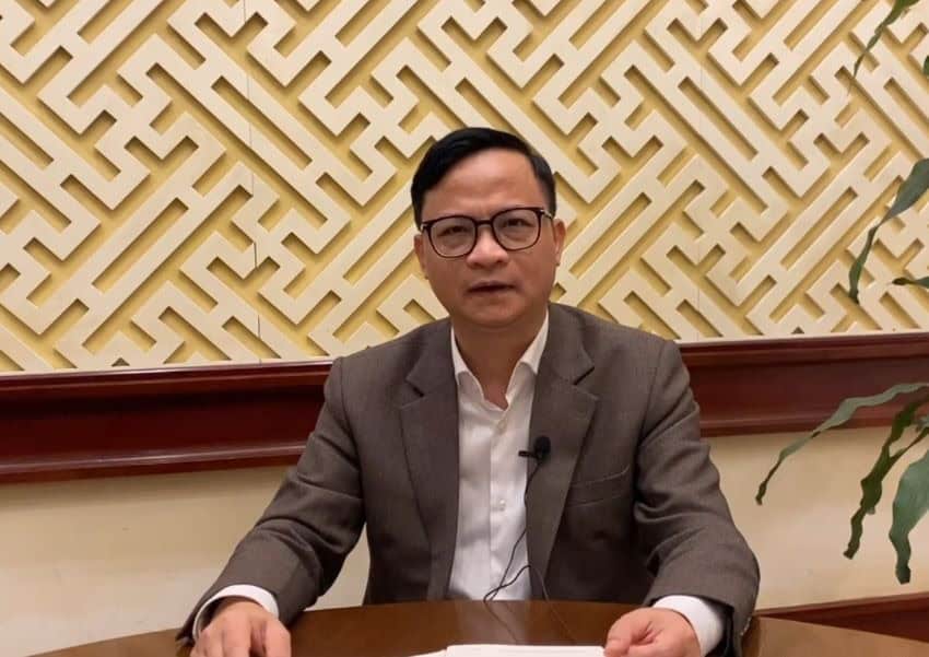 A man wearing a brown blazer sitting at a desk.