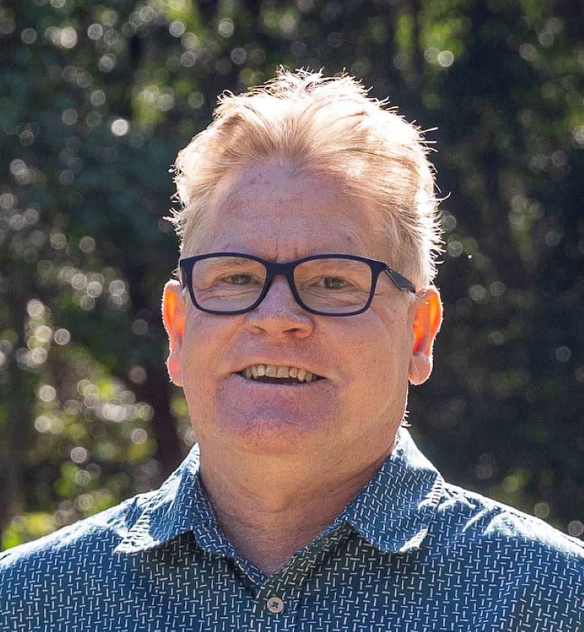 Headshot of a man wearing black rimmed glasses and a blue shirt.