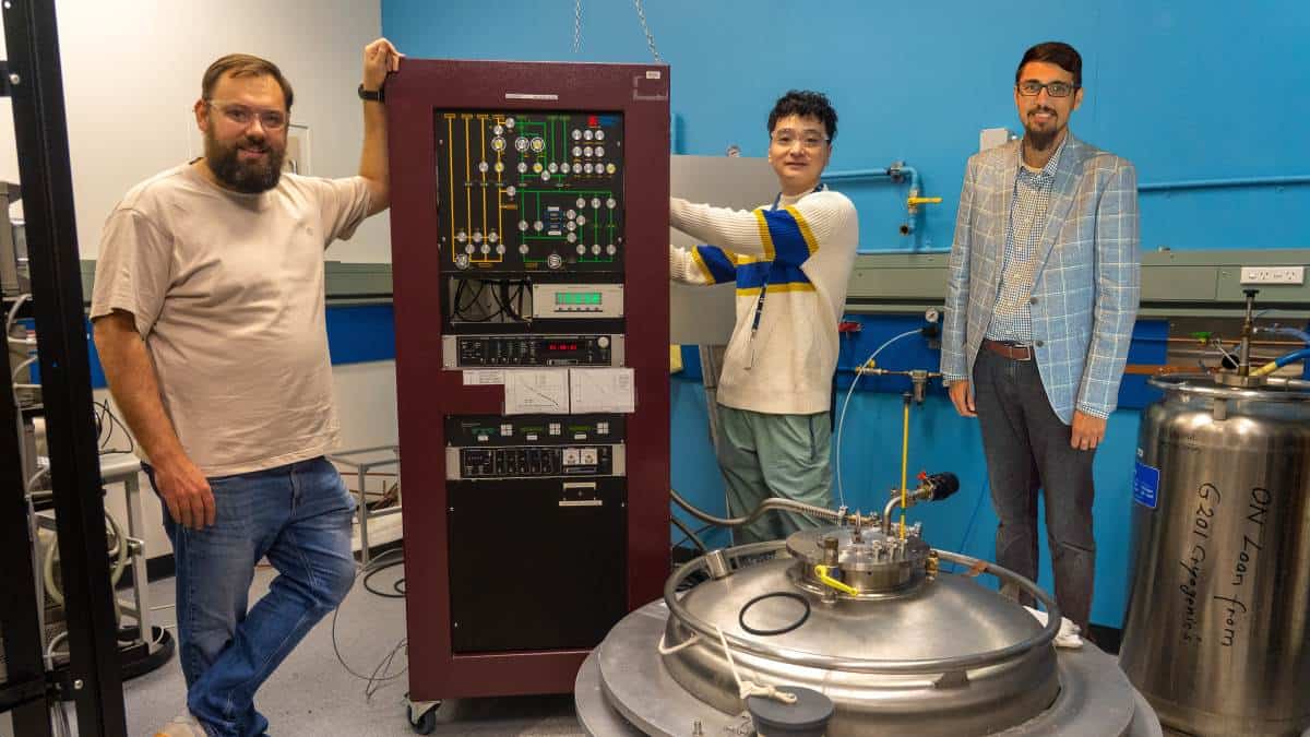 Three researchers with quantum bit control unit in lab with blue wall