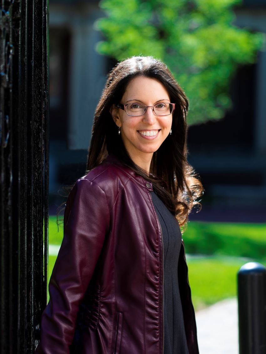 Woman in a purple jacket stands side on with trees in the background