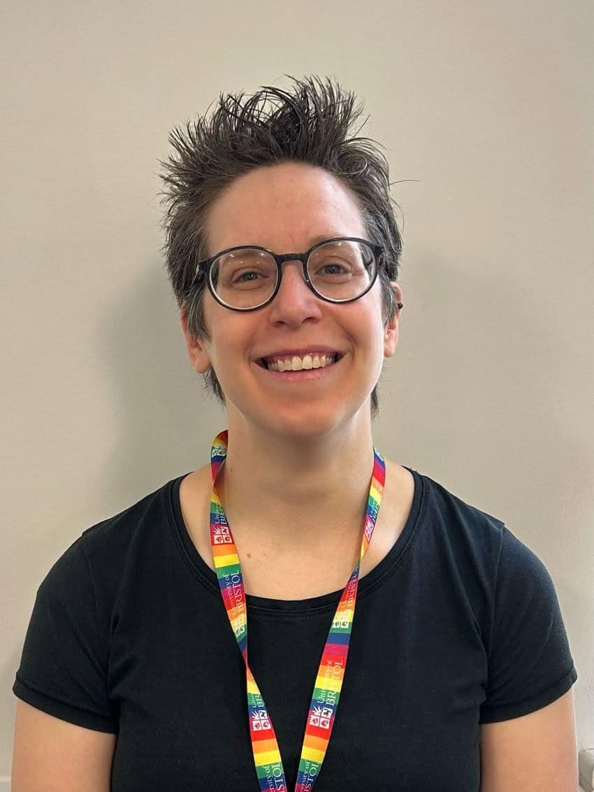 Headshot of a woman weariing glasses a black t-shirt and rainbow lanyard.